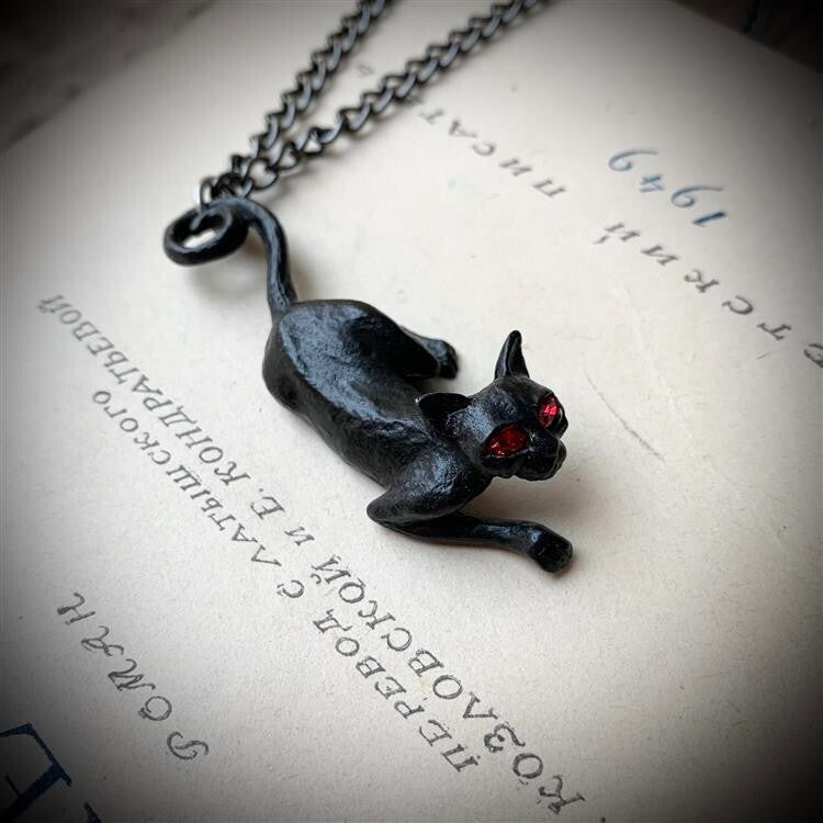Black cat pendant necklace on a textured surface with text