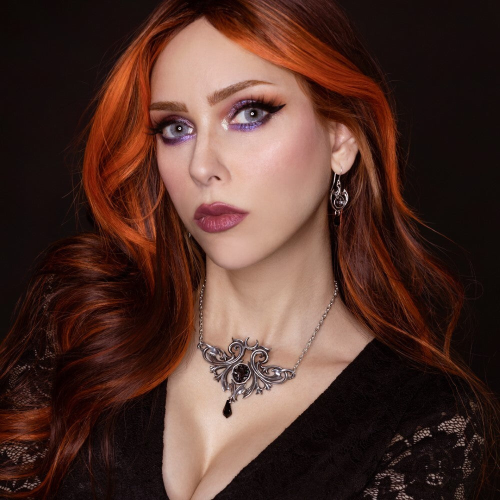 Woman with red hair and purple eye makeup wearing a black top and silver necklace.