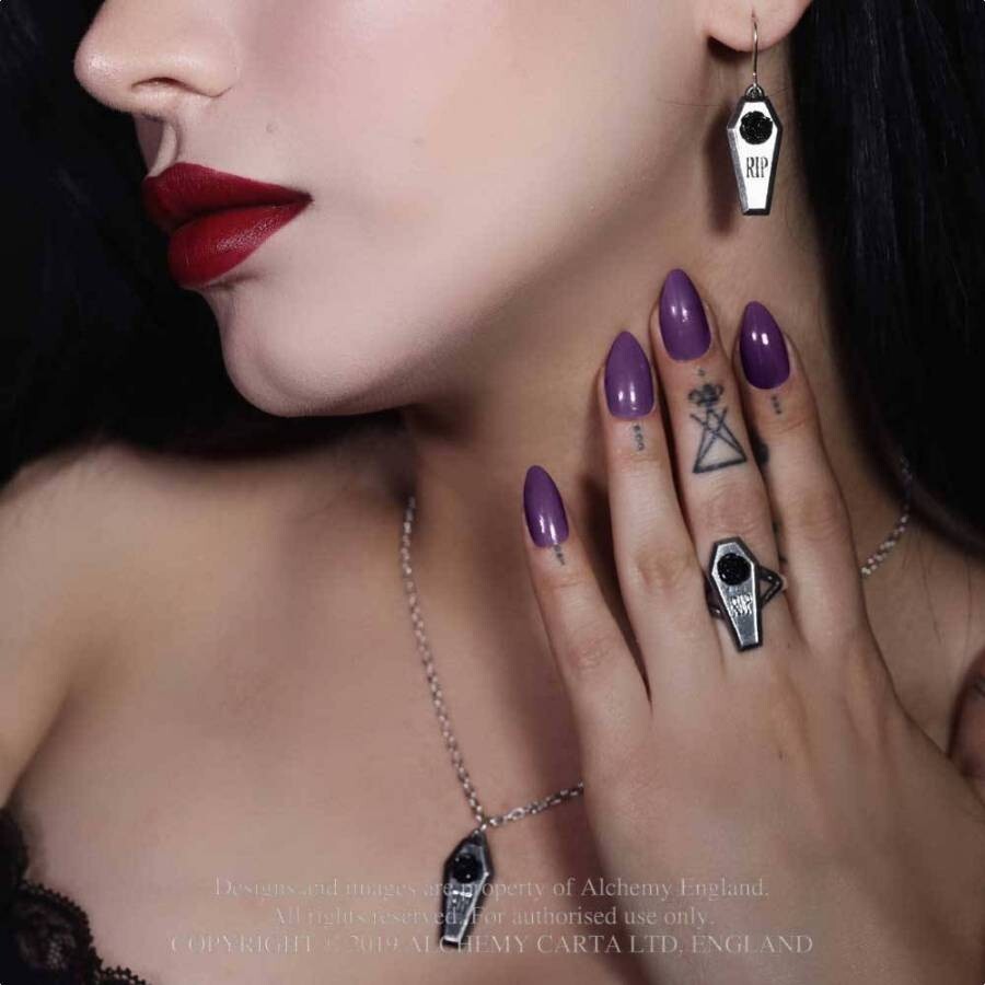 Close-up of a woman's face and hand with purple nail polish and coffin-shaped jewelry.