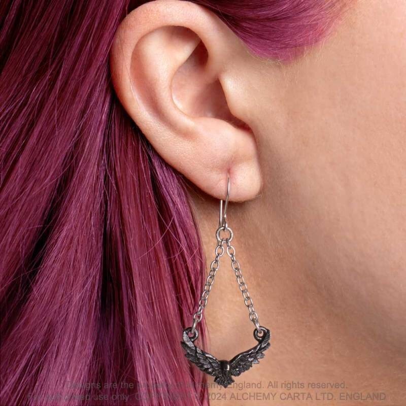 Close-up of an ear wearing a dangling silver earring with a chain and wing design, against a blurred background.