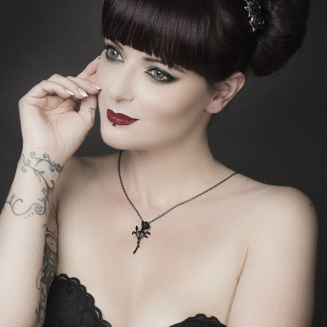 Woman with dark hair and tattoos wearing a black dress against a dark background