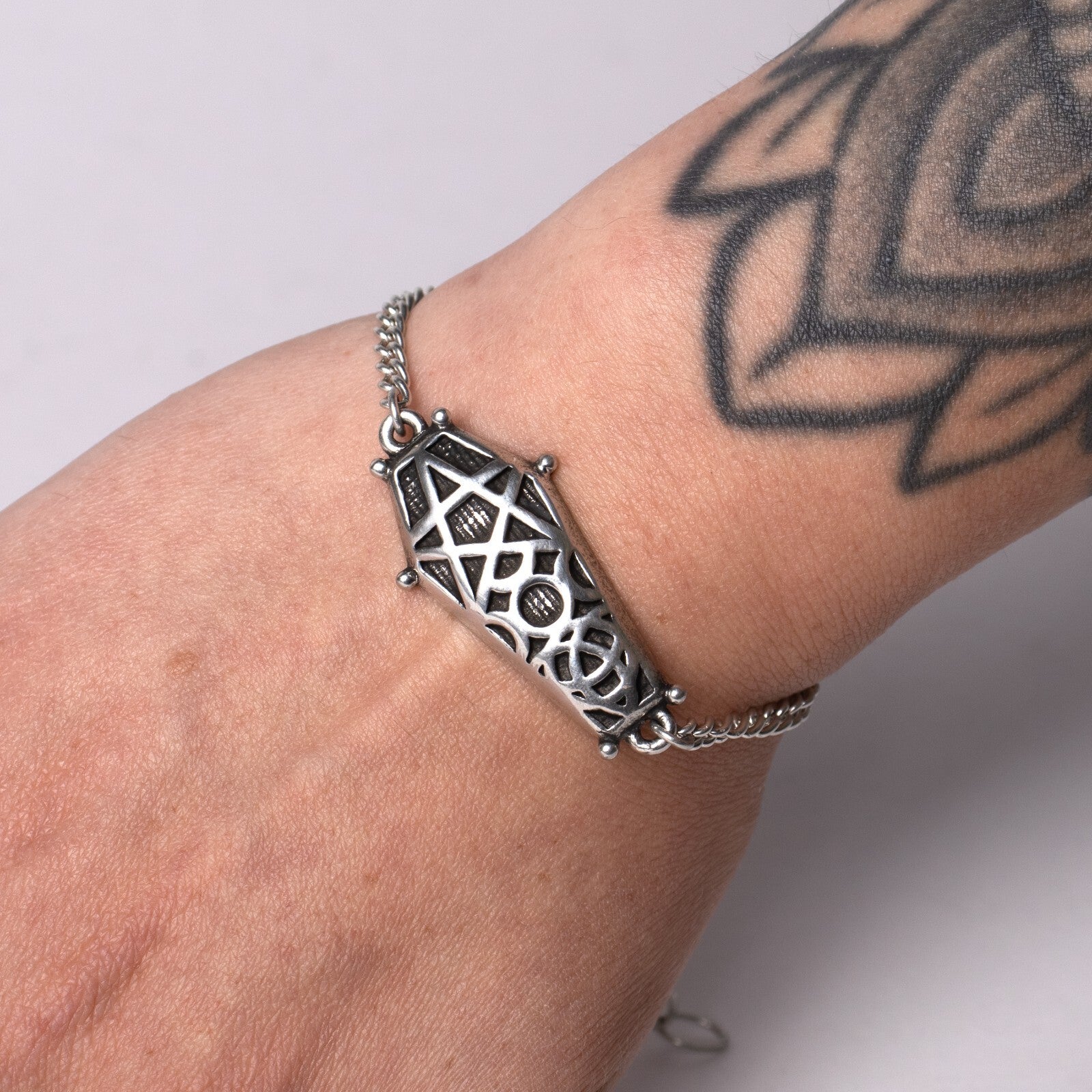 Silver bracelet with intricate design on a wrist with tattoos