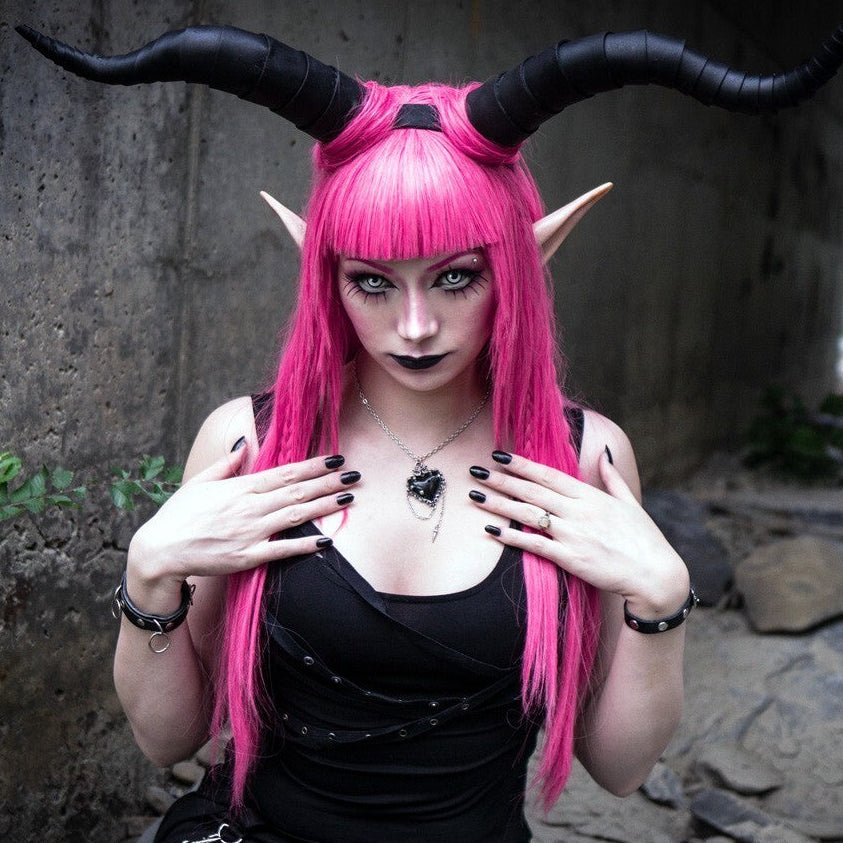 Person with pink hair and black horns posing outdoors.
