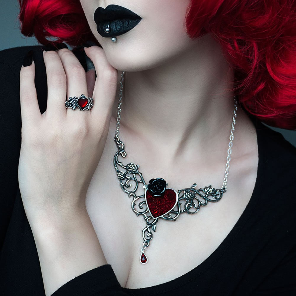 Person wearing a necklace with a red heart pendant and black rose design, holding a red flower.