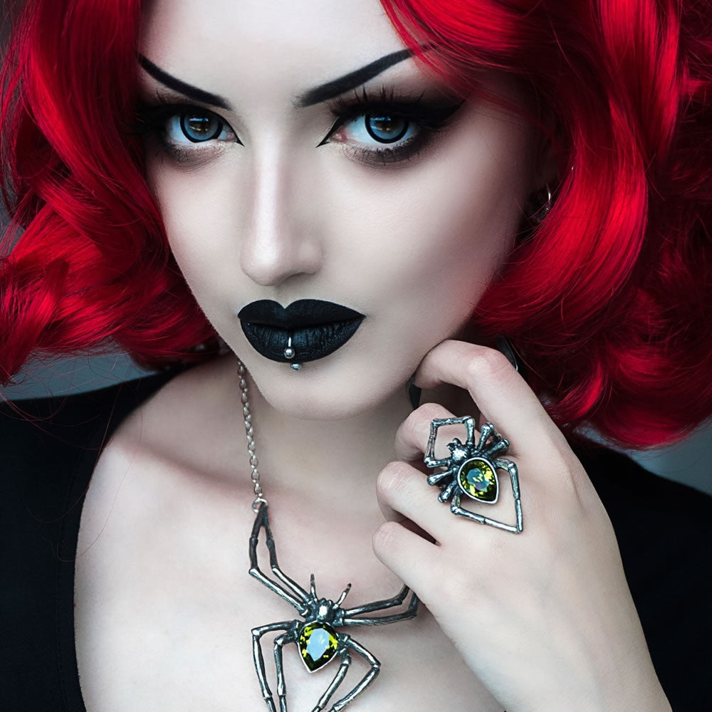 Woman with red hair and black lipstick wearing a spider necklace and ring.