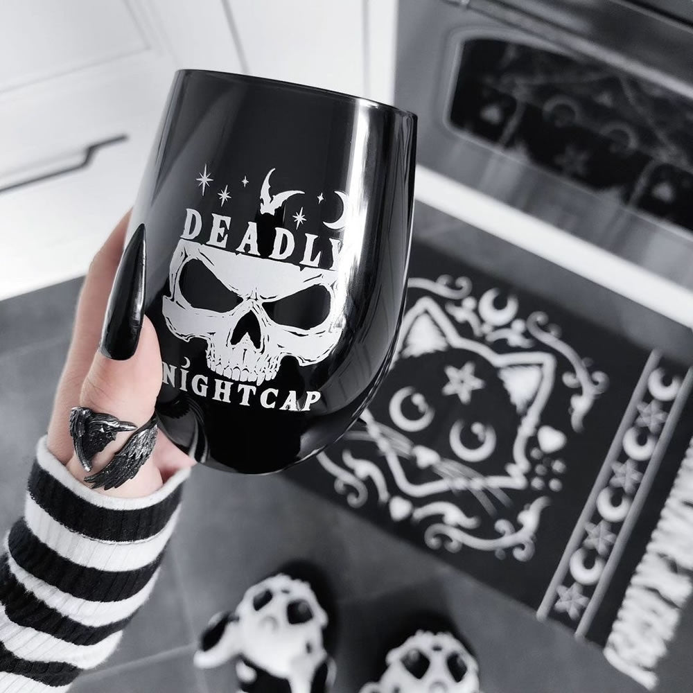 Black mug with skull design and 'Deadly Nightcap' text held by a person in a kitchen.