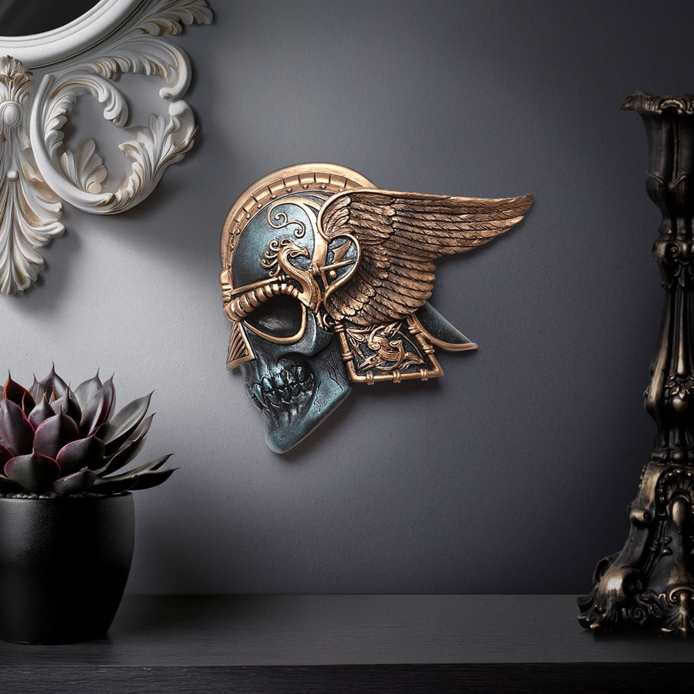 Decorative wall piece with skull and wings on a dark gray wall.